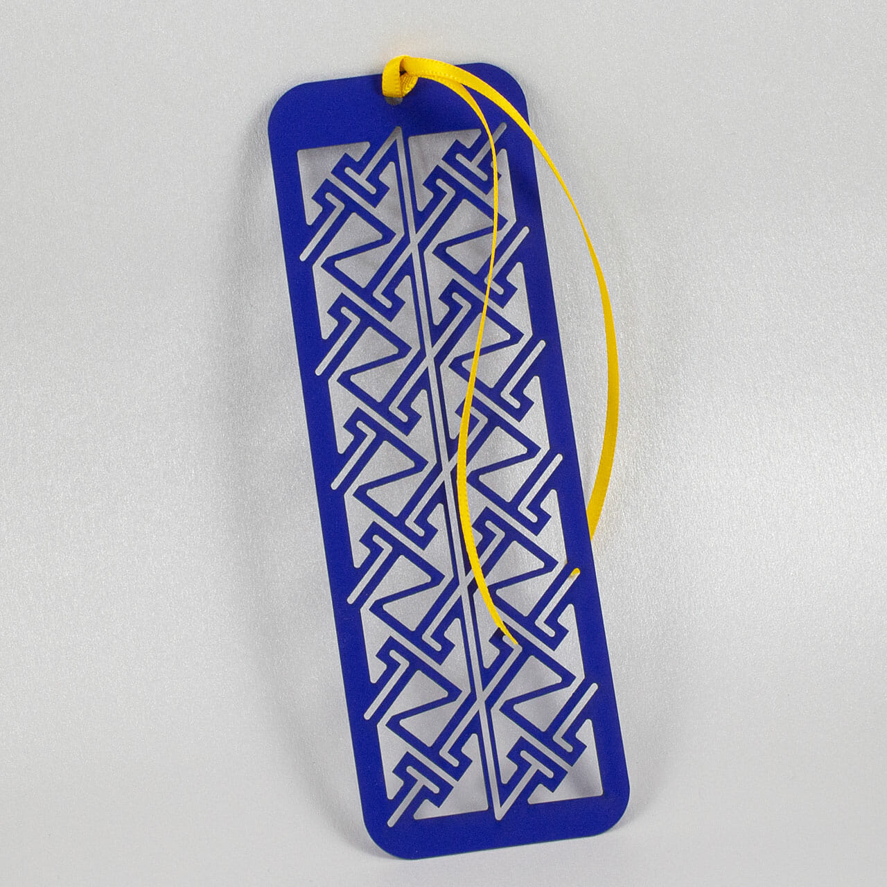 Kirigami bookmark with a Celtic key pattern cut from cobalt blue stock with a yellow ribbon tied to one end.