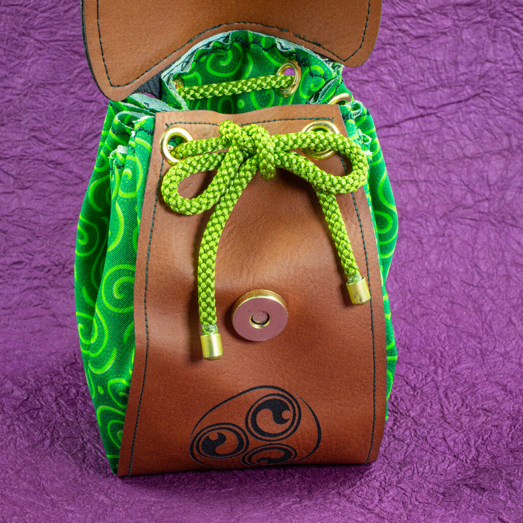 A small fantasy/Medieval belt pouch. The main body is cotton fabric printed with interlocking Celtic spirals in various shades of green. The front, bottom, back and flap are medium brown faux/vegan leather. The flap is open, showing a green braided kumihimo drawstring with brass aglets and a brass magnetic closure.