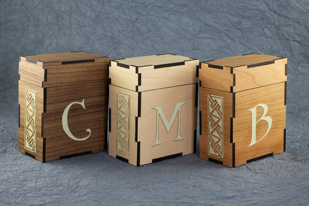 Standard size deck boxes for M:tG and similar games. There is a Celtic key pattern panel engraved on the left sides and initials on the fronts (C, M and, B). These boxes are made from (left to right) walnut, maple and, cherry plywood.