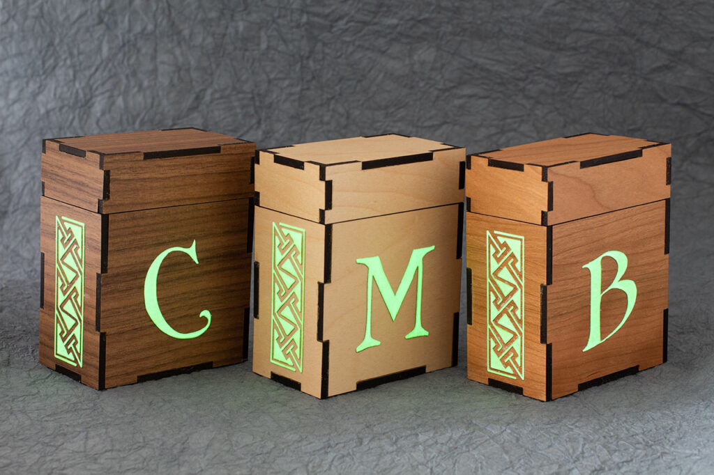 Standard size deck boxes for M:tG and similar games. There is a Celtic key pattern panel engraved on the left sides and initials on the fronts (C, M and, B). These boxes are made from (left to right) walnut, maple and, cherry plywood.