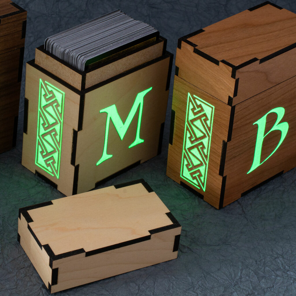 Standard size deck boxes for M:tG and similar games with glowing engravings. There is a Celtic key pattern panel on the left sides and initials on the fronts (M and B). The left box has the lid removed, showing a deck inside.