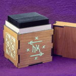 Wood sleeved "commander" deck box for M:tG and similar games with glowing engraved designs: an embellished Futhark rune on the front and, a Celtic key pattern panel on the left side. Lid removed, showing a sleeved deck inside.