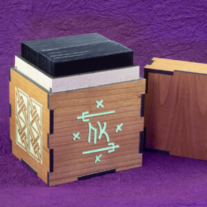 Wood sleeved "commander" deck box for M:tG and similar games with glowing engraved designs: an embellished Futhark rune on the front and, a Celtic key pattern panel on the left side. Lid removed, showing a sleeved deck inside.