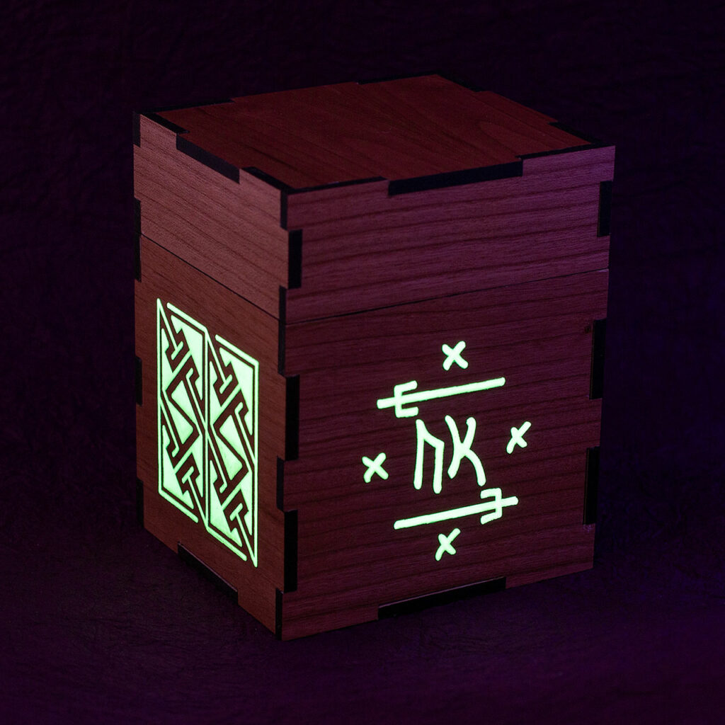 Wood sleeved "commander" deck box for M:tG and similar games with glowing engraved designs: an embellished Futhark rune on the front and, a Celtic key pattern panel on the left side. Seen here in low light with the engraves glowing.