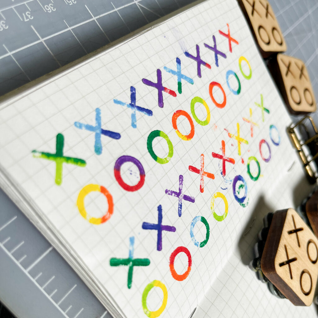 Two columns of multi-color impressions from the XOXO stamps fill a page in a small grid notebook