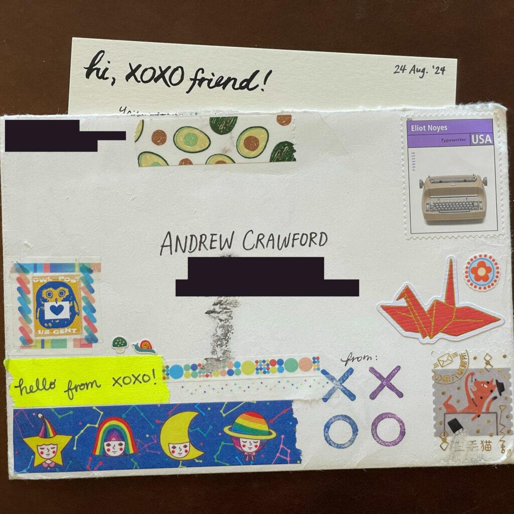 An envelope Addressed to Andrew Crawford (rest of the address and return address redacted), decorated with stickers and stamps. A card behind reads hi, XOXO friend!