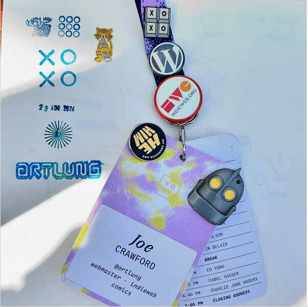 Joe Crawford's XOXO badge with pins and stickers on a stamped piece of paper