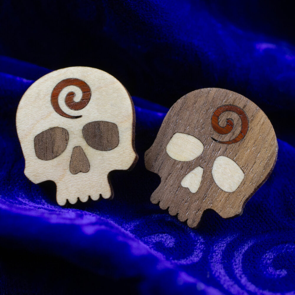 Godar Blot skull pins – hardwood inlay skull pins from white oak, walnut and, padauk. The white oak is dominant on one pin and the walnut is dominant on the other.