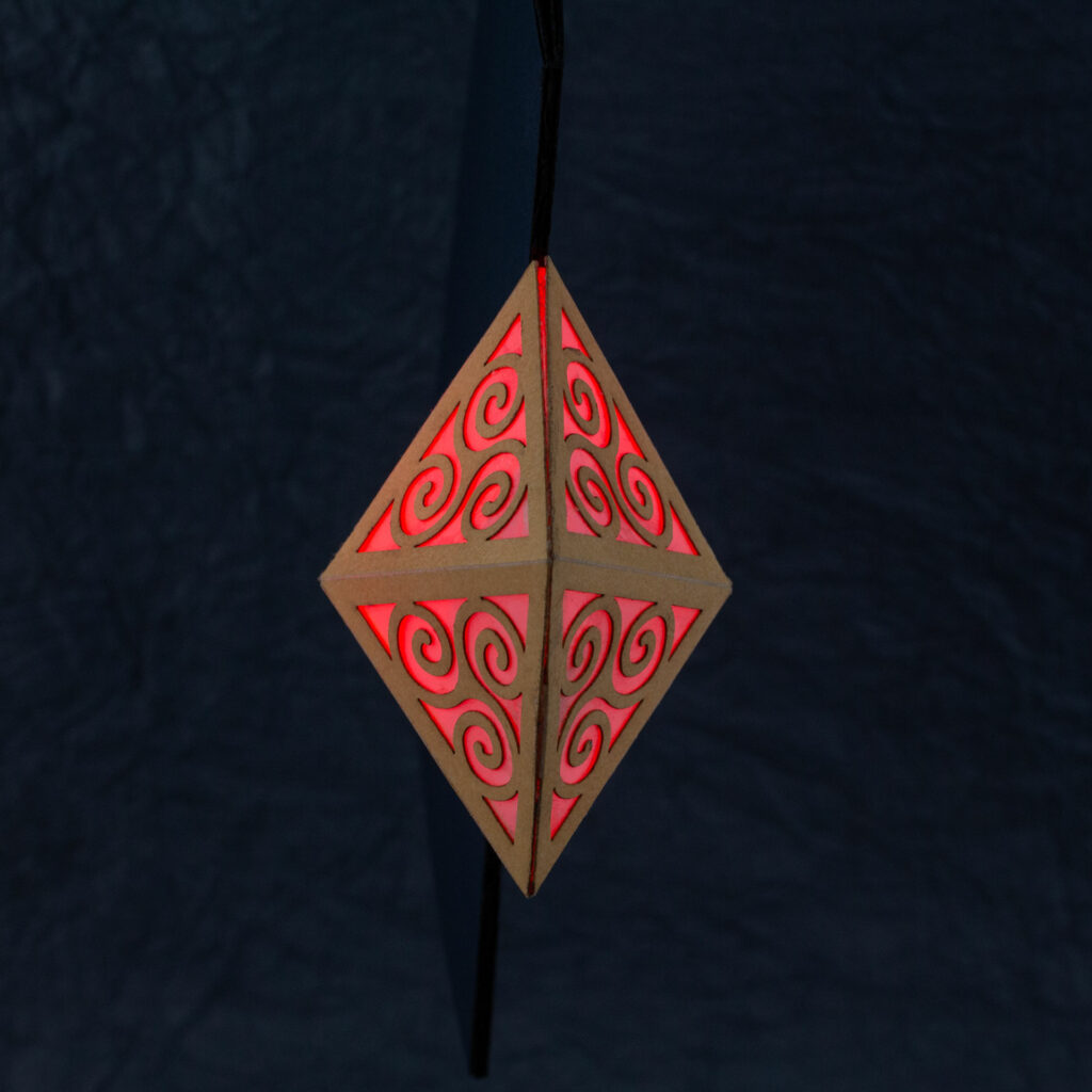 Top-down view of the Spiral Crystal pop up card. Four panels with Celtic triskelion designs appear to make a diamond pattern, perched on the edge of a blue card.