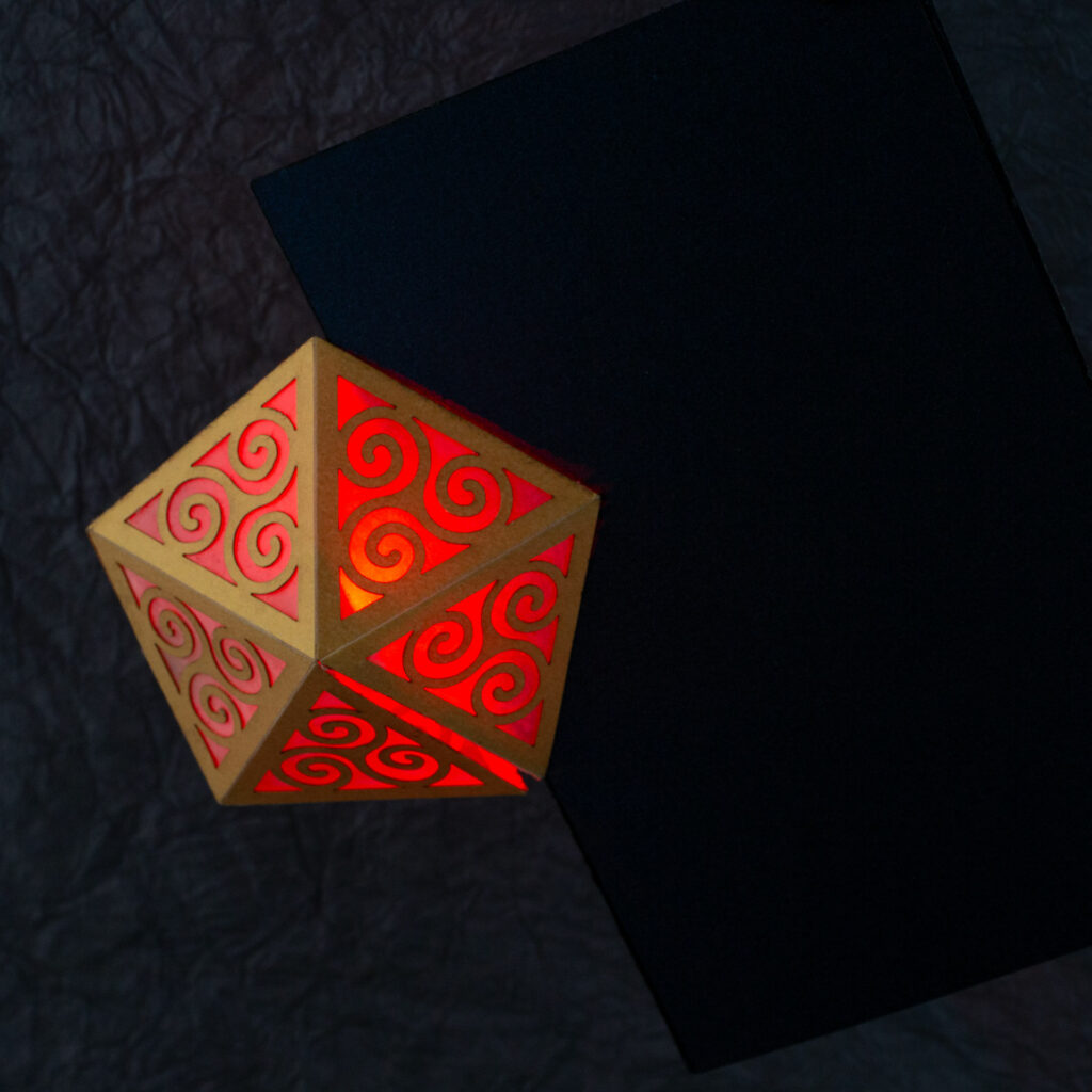 Spiral Crystal pop up card fully open (360º). A yellow pentagonal lattice with triangular panels featuring Celtic triskelion designs is lit from within by a red light. The base card is a dark blue.