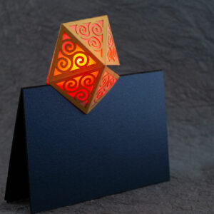 Spiral Crystal pop up card fully open (360º). A yellow pentagonal lattice with triangular panels featuring Celtic triskelion designs is lit from within by a red light. The base card is a dark blue.