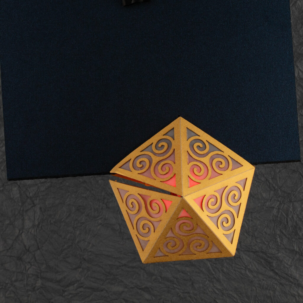 Spiral Crystal pop up card fully open (360º). A yellow pentagonal lattice with triangular panels featuring Celtic triskelion designs is lit from within by a red light. The base card is a dark blue.