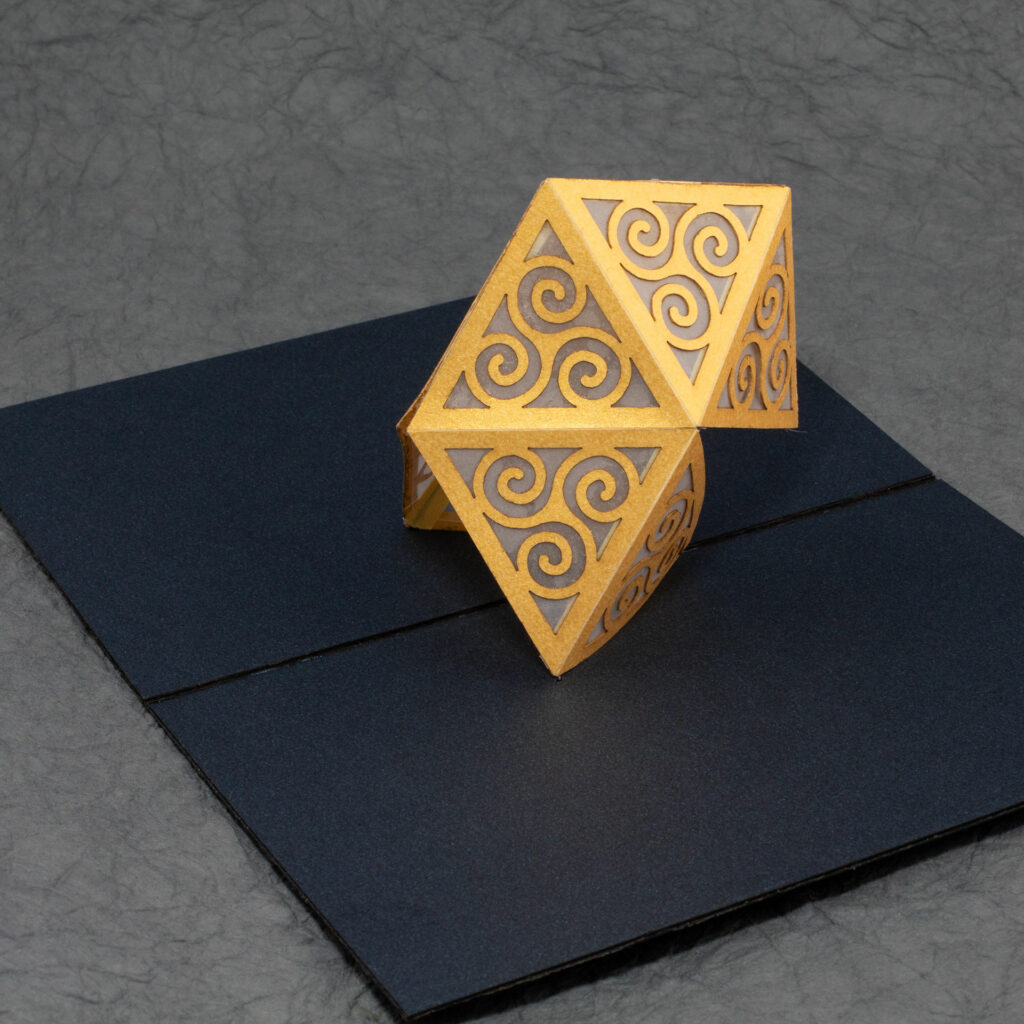 A dark blue card with an attached yellow-gold structure composed of triangular panels with Celtic triskelion designs.