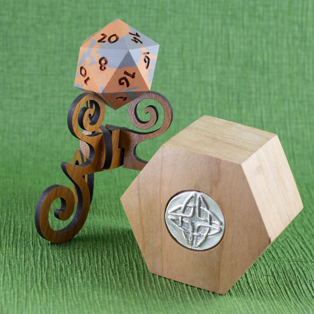 Cherry Hex Chonk Box with a silver Celtic knotwork medallion in the lid, in front of a walnut stand with a silver and copper 20-sided Jesmonite die.