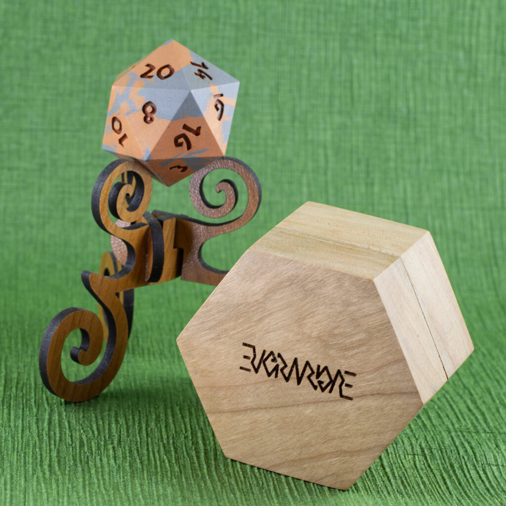 Cherry Hex Chonk Box with the Evermore ambigram engraved on the bottom, in front of a walnut stand with a silver and copper 20-sided Jesmonite die.