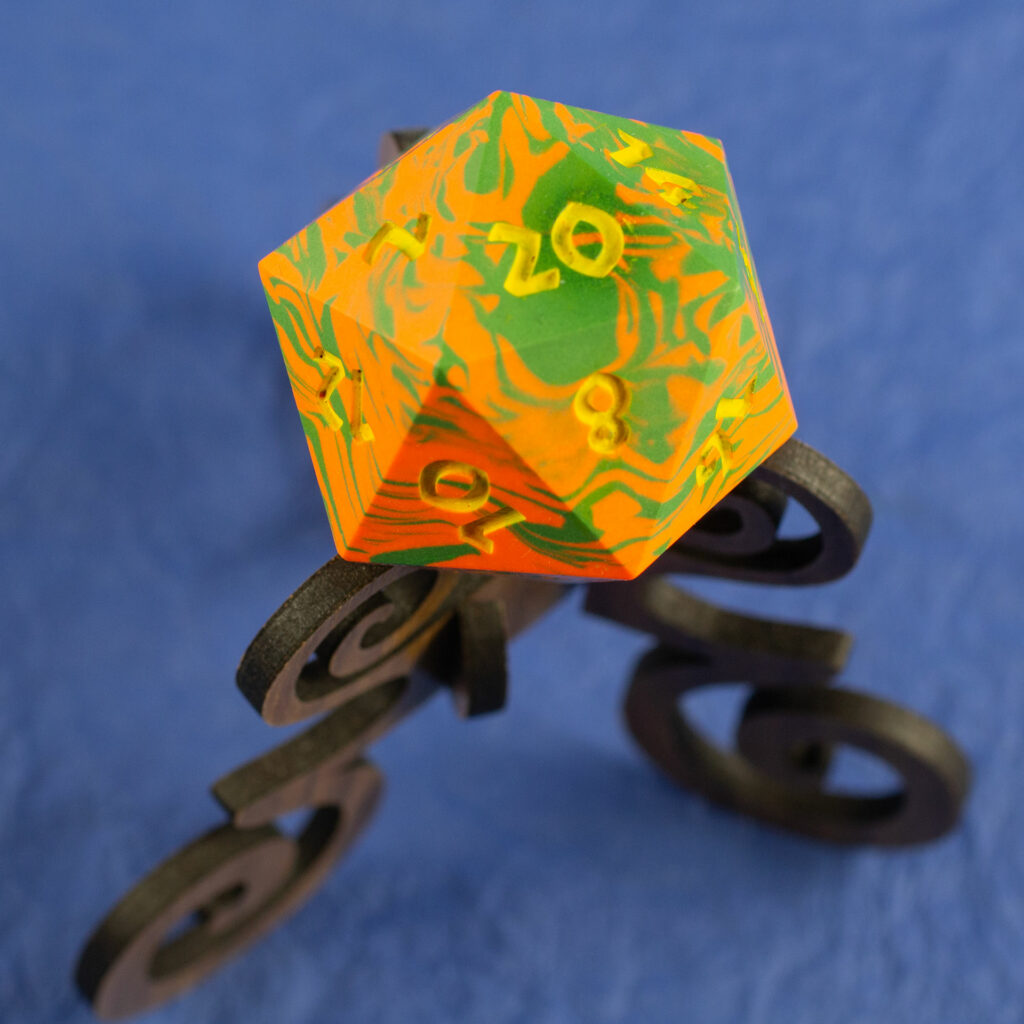 Top view of a green and orange 42mm Jesmonite 20-sided die with the numbers painted in yellow on a walnut stand.