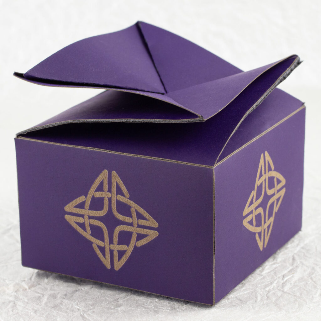 A small, squat, square, deep violet twist-top box with a Celtic knot engraved in a pale brown on each side.