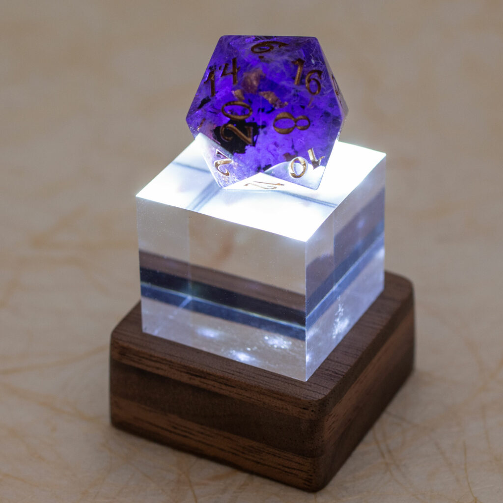 Small light-up stand with a standard 22mm 20-sided resin die in shades of deep purple with gold flakes and numbers.