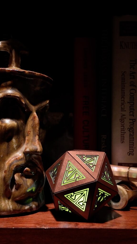 Copper rechargeable icosahedron with yellow light sits on a bookshelf with a ceramic Thor face jar and a pair of old pearl-and-brass opera glasses