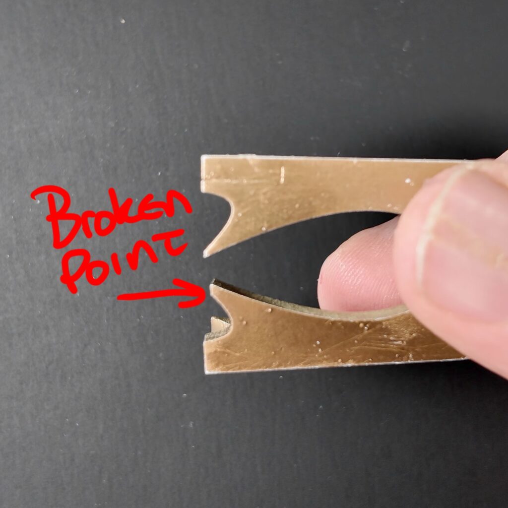 Two curved legs painted gold being held up against a black background to show how a point has broken off of one of them.