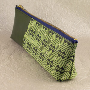 Three-quarter view of a pencil pouch that is about two-thirds fabric printed with a Celtic key pattern design in green, and one-third green cactus leather. A blue and brass zipper closes the top. The surface and background are a pearlescent white crumpled-finish paper.