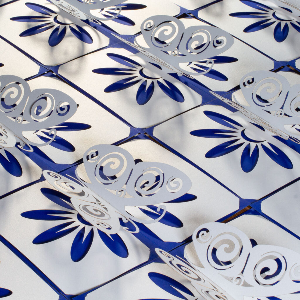 A collection of somewhat stylized kirigami pop up pearlescent white paper butterfly cards arranged side-by-side. The butterflies have Celtic spiral designs cut into the wingss. There is a flower design cut into the base, which allows the cobalt blue backing card to show through for the petals. Three-quarters above left view.