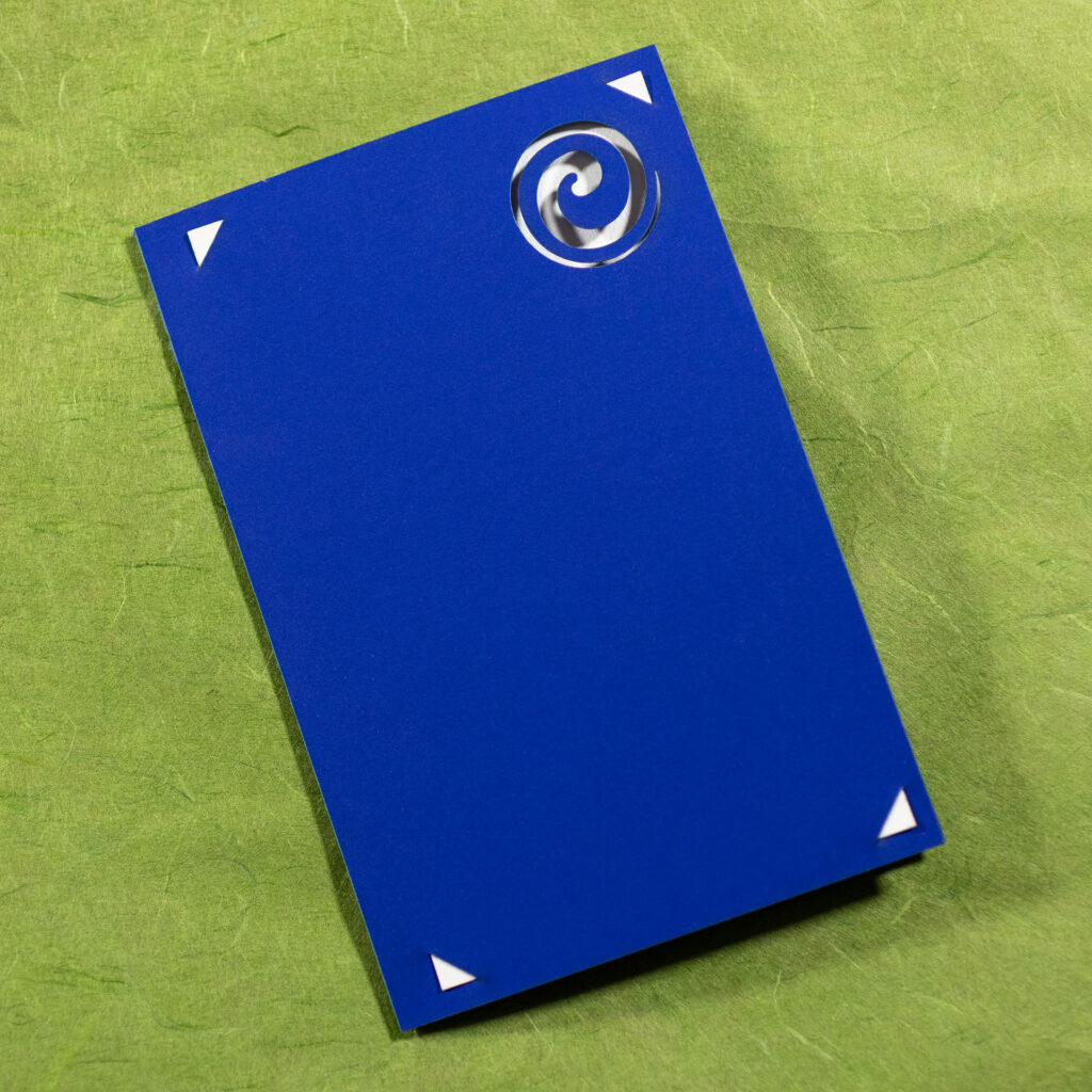 Closed cobalt blue card with a spiral cut out in the upper right corner showing the white paper inside. There are also little triangles in the corners where the corners of the interior pieces come through to mount them.