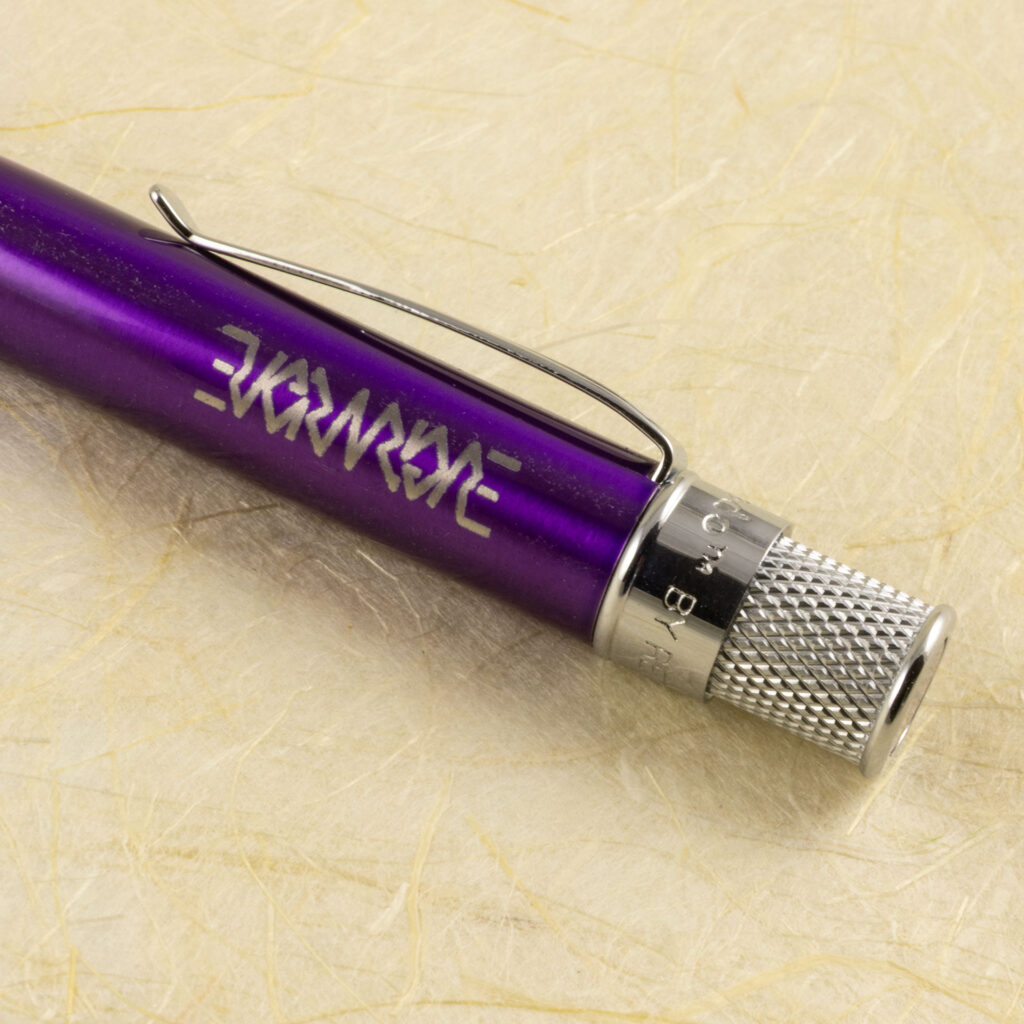 Close-up of the Evermore ambigram engraving on the end of a purple lacquered metal pen.