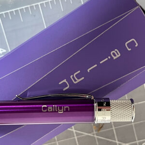 Close-up of the end of a purple Retro 51 Classic Lacquer pen engraved with the name Cailyn, lying on top of a purple box engraved with the same name.