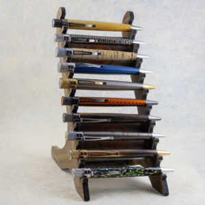 A pen rack made of walnut hardwood with two parallel angled vertical pieces connected by three flat cross members. The front-facing edges are serrated to hold 10 pens. The two front-facing cross members are inlaid with an off-center Celtic spiral made of padauk hardwood. The rack contains ten Retro 1951 pens (curvy, retro-future design shape with knurled twist-to-open tops, pen clips, in a variety of materials and finishes). Three-quarters left-side view.