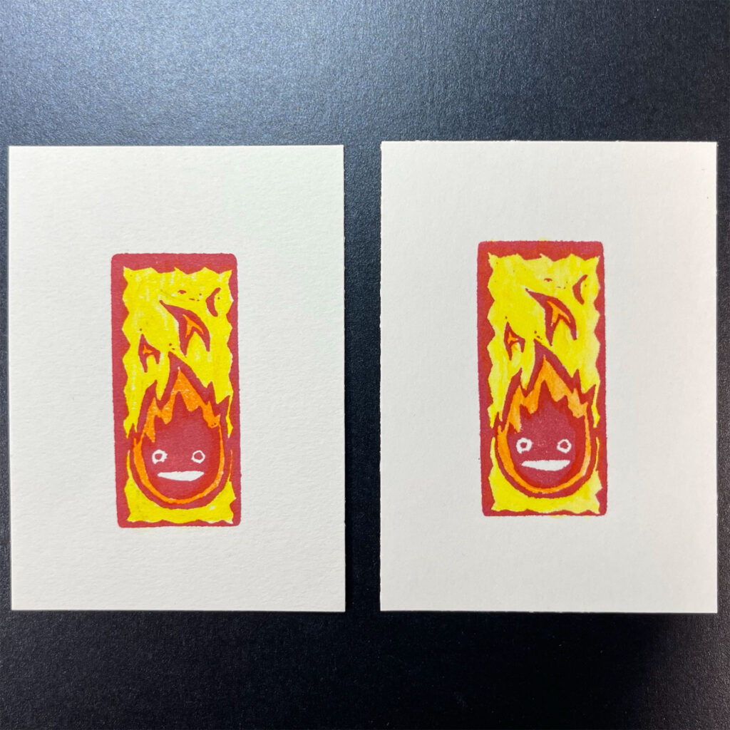 Comparison of finished mixed-media Calcifer prints showing that the added watercolor pencils are a little more vibrant on the Strathmore paper (right) than the Bristol (left).