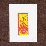 A white rectangle of paper imprinted with Calcifer, a stylized flame with two eyes and a mouth. The print has also been colored in with yellow and orange watercolor pencils. The print is signed with a small A and is resting on a background of crinkled brown paper (momigami).
