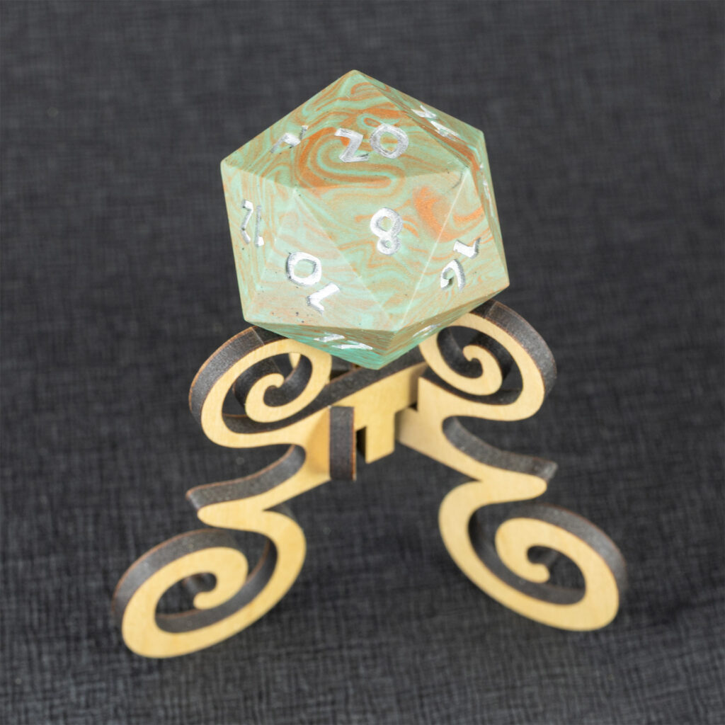 Three-quarters top-down view of a large (42mm) 20-sided die (d20) swirled with teal an copper with the numbers painted in with metallic silver, resting on a three-legged stand with spiral elements made from maple. The 20 side is facing up, with the 2, 8, 10, 12, 14, 16, and 17 faces visible. The background is a black creped paper (chirimen).