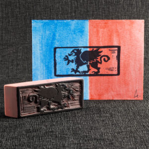 The left half of a landscape-format piece of paper has been colored blue with watercolor paint, and the right half red. Stamped in black is a left-facing griffin (a beast with the head, wings, and front claws of an eagle, and the body of a lion) passant (standing flat with one claw raised) surrounded by a rectangular border. The carved pink eraser stamp that made the impression , stained with black ink, is standing on one long edge in front of the lower left corner of the print. The background is handmade black crepe paper (chirimen).