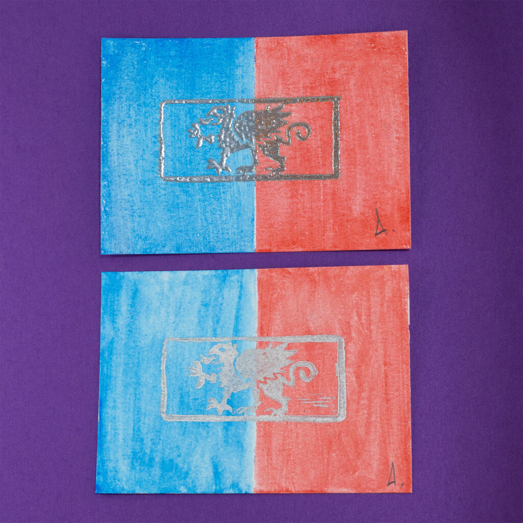 Two prints for comparison. For each, the left half of a landscape-format piece of paper has been colored blue with watercolor paint, and the right half red. Each is printed with a left-facing griffin (a beast with the head, wings, and front claws of an eagle, and the body of a lion) passant (standing flat with one claw raised) surrounded by a rectangular border.The top print is embossed in silver. The bottom is printed with a flatter metallic silver ink. The prints are signed with a stylized A in the lower right corner. The background (behind the prints) is purple.